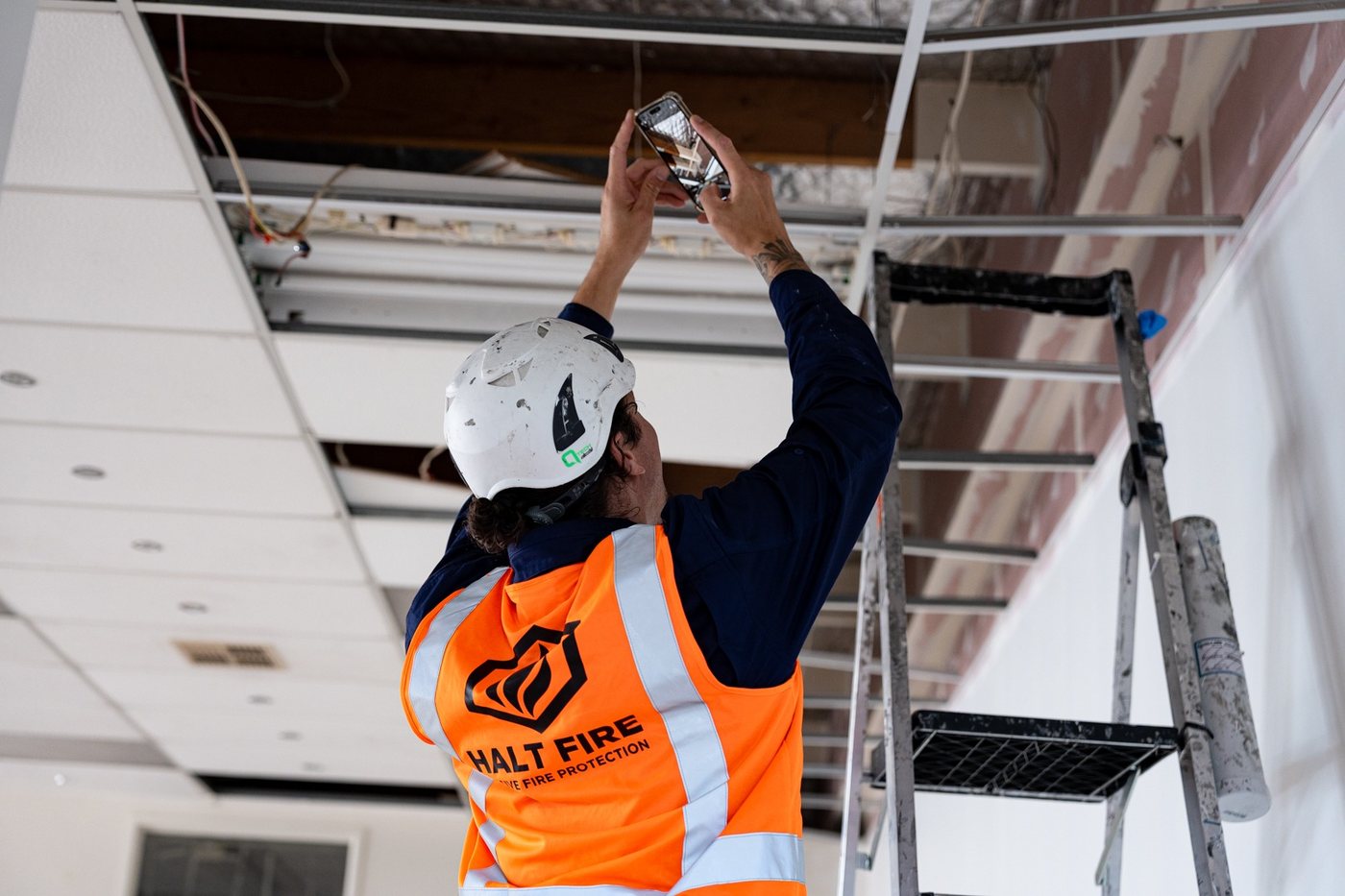 Halt Fire installer sealing a service penetration above a ceiling grid on an Auckland commercial site
